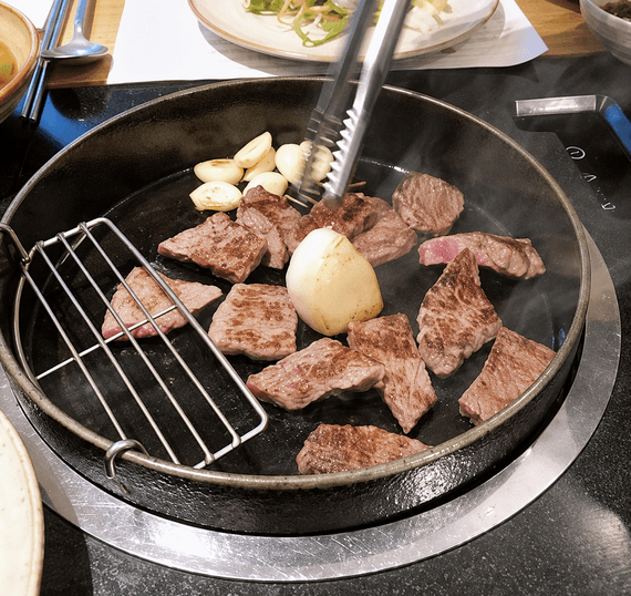 Hanwoo beef grilling on a table grill, with garlic and a soft-boiled egg.