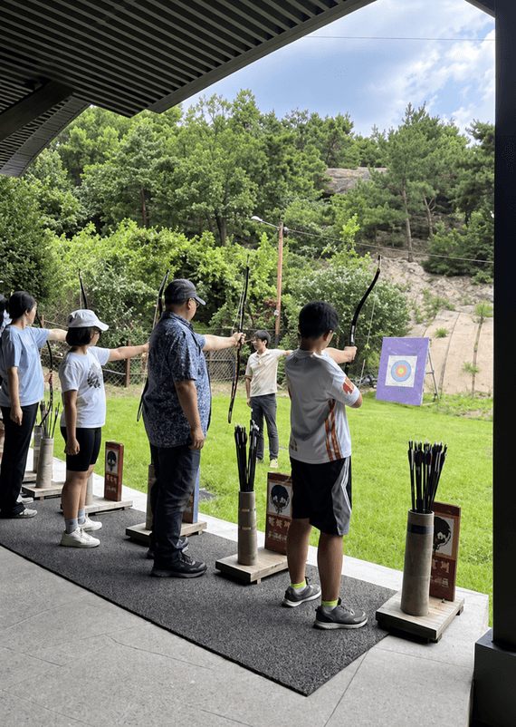 Archers on the shooting line at an outdoor traditional Korean archery range.