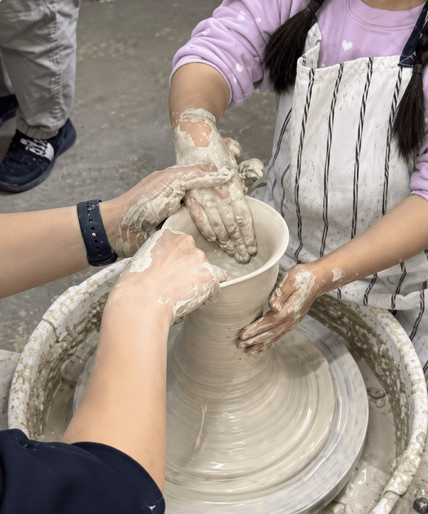 Hands shaping a vessel on a potter's wheel in a studio.