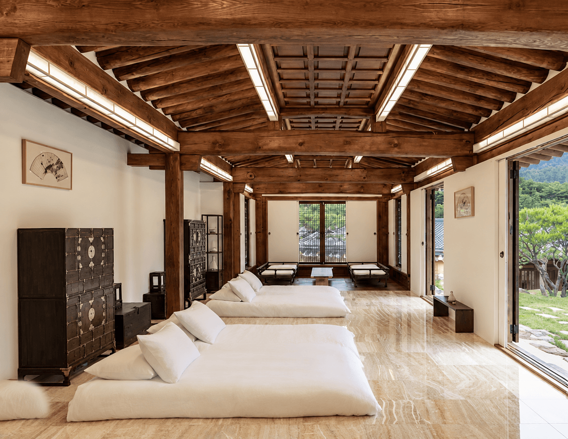 A row of beds under the exposed timber beams of a restored hanok room.
