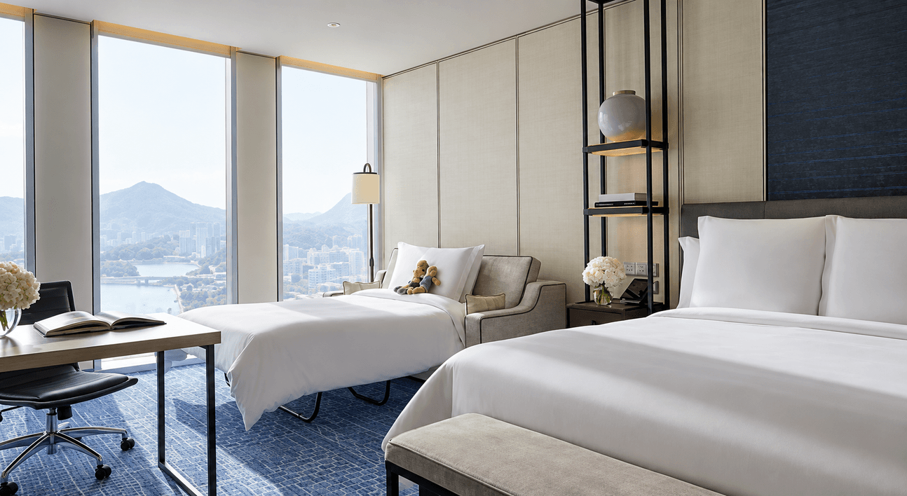 A hotel room with two beds, a desk and a tall window looking out over the city.